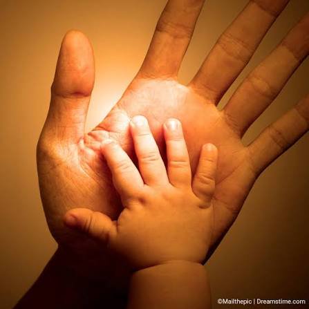 Close-up of a tiny baby hand resting on the open palm of a larger adult hand, warm glowing golden...