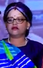 Portrait of a woman with glasses wearing a purple headscarf and blue outfit on stage.