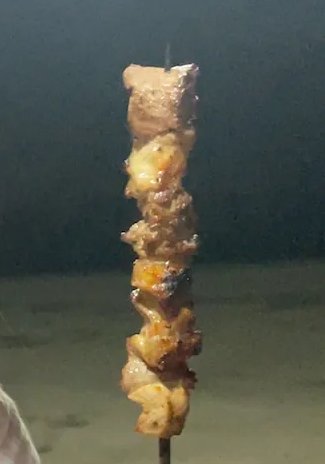 Skewered grilled meat chunks on a bamboo stick with a smoky, charred finish
