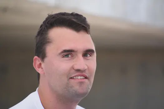 Close-up portrait of a smiling man in a white shirt outdoors with a blurred background.