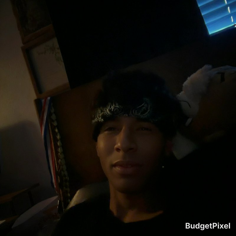 Dim casual selfie of a young man wearing a patterned paisley bandana, relaxing in a low light bed...