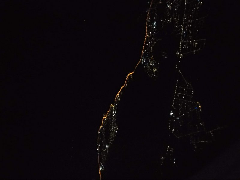 Night satellite view from space of glowing coastal city lights tracing a shoreline against dark o...
