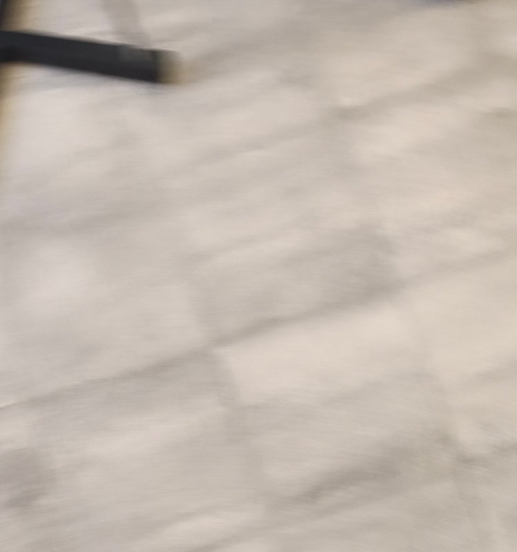 Motion-blurred view of light cream marble tile flooring, with a dark furniture leg visible in the...