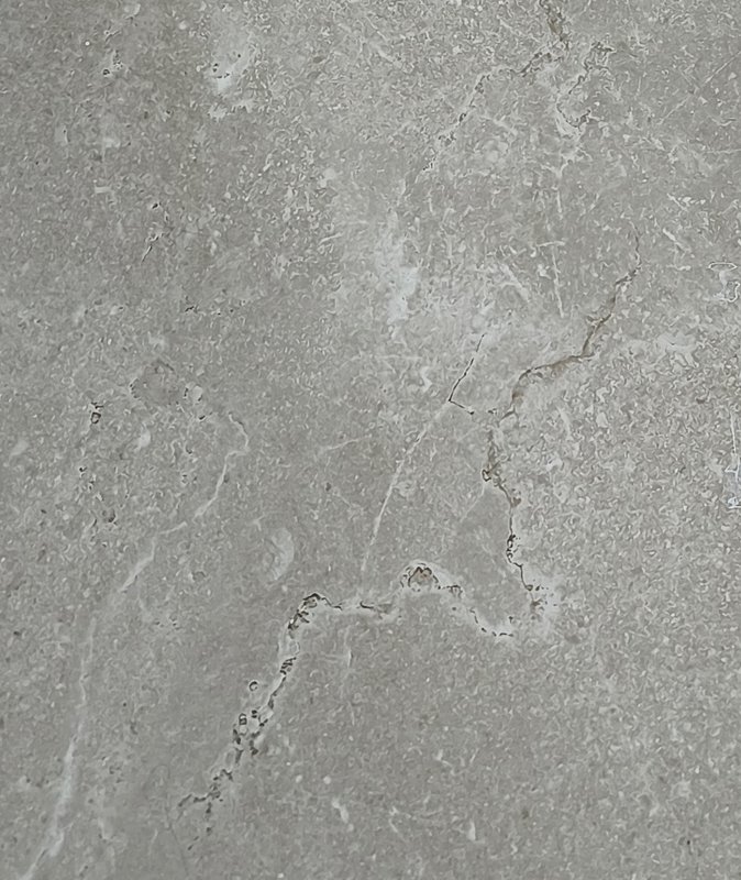 Close-up of a natural light grey marble surface with delicate irregular warm veining and subtle t...