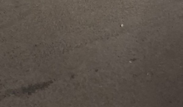 Matte warm taupe textured concrete surface with faint scuff marks and tiny scattered debris specks