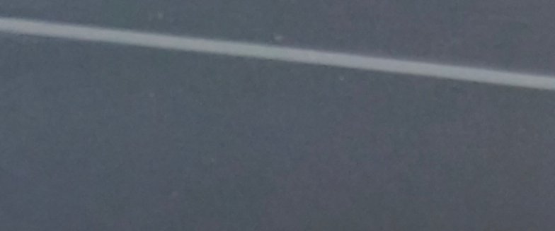Straight pale white lane marker line running diagonally across dark gray asphalt road surface.