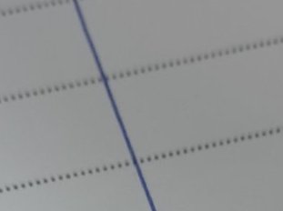 Close up of ruled notebook paper, with a diagonal blue margin crossing horizontal dashed guide li...