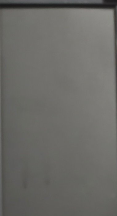 Blurry low-light view of a plain blank vertical off-white panel with a thin dark top frame border