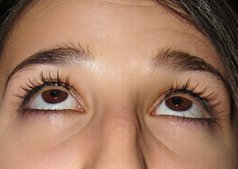 Extreme close up of wide brown human eyes looking upward, with long lashes and full dark eyebrows.