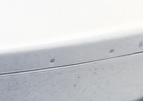 Close-up of brushed silver metal panel with two Phillips head screws, thin horizontal seam, and b...