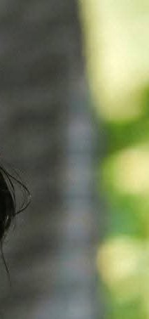Close-up partial shot of a person’s dark hair against a blurred green-yellow background.