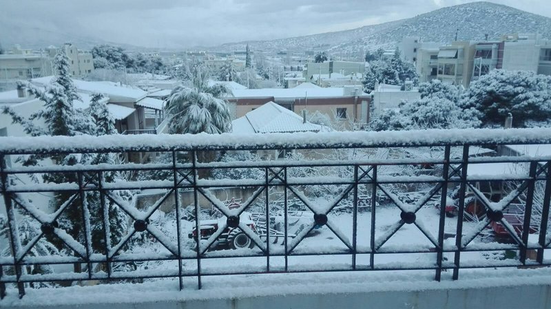 Snow-covered balcony view overlooking a suburban neighborhood with frosted rooftops and hills in the distance.
