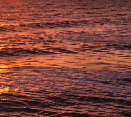 Rippling ocean water glows with warm orange sunset light across gentle small waves