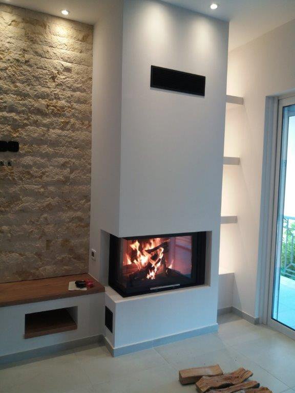 Modern white fireplace with glass front in a bright living room featuring a stone accent wall and built-in bench.