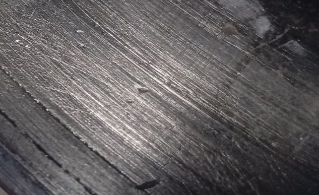 Macro close-up of worn brushed dark metal surface covered in diagonal scratch and grind marks wit...
