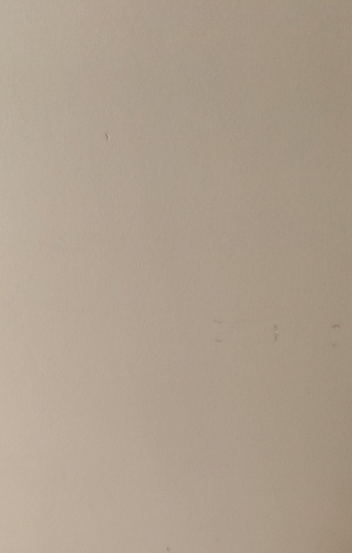 Plain smooth warm light beige matte wall with faint small scuff marks and tiny dust flecks scatte...