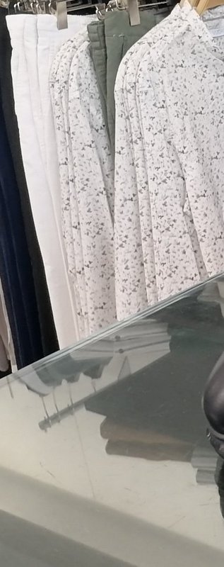 Clothing rack holding casual neutral tops and pants above a clear glass retail display counter