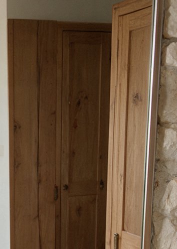 Paneled light pine wooden door reflected in a full length leaning mirror next to a rough natural ...