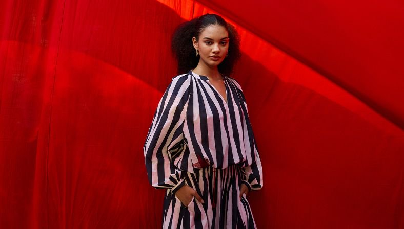 Woman in black-and-white striped outfit posed against a vivid red fabric backdrop.