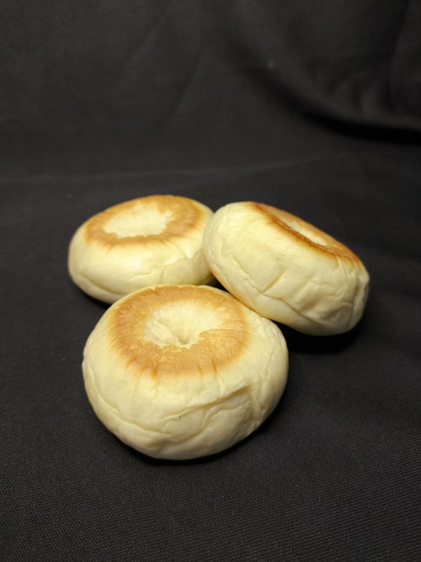 Three plump soft baked buns with golden toasted ring tops arranged on a dark textured black fabri...