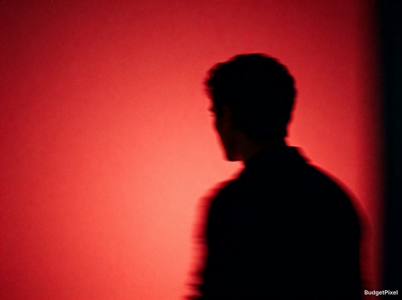 Motion-blurred profile silhouette of a man, set against a soft glowing deep red gradient background.