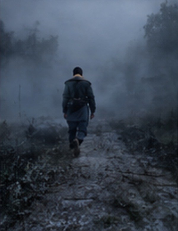 Lone hiker walks away along a muddy fog-shrouded forest trail