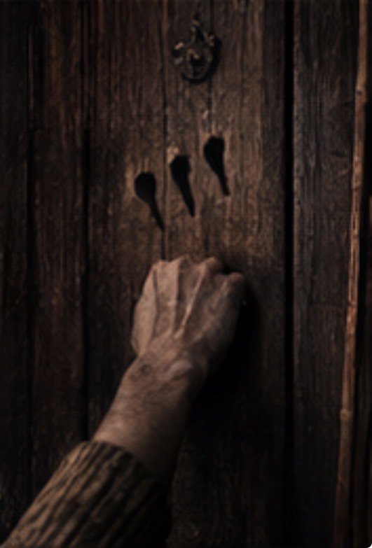 Pale hand rests against an old wooden door with three deep claw-shaped indentations above it