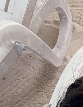 White plastic beach chair on sandy shore with a partial view of a person.