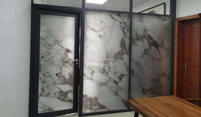 Modern office interior with black-framed glass partitions featuring marble-pattern frosted panels...