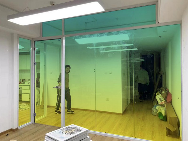 Person near a glass office partition with a green-to-yellow tinted wall in a modern interior.