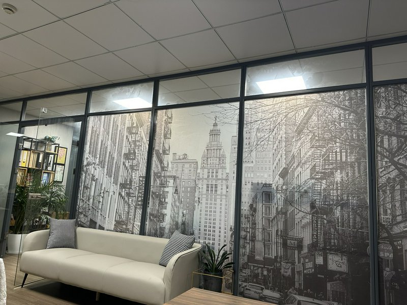 Modern office lounge with white sofa and black-and-white cityscape mural on glass panels.