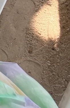 Close-up of sandy ground with footprints and colorful pastel fabric in the corner.