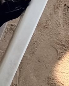 Close-up of a white plastic playground slide on sandy ground with a shadow.