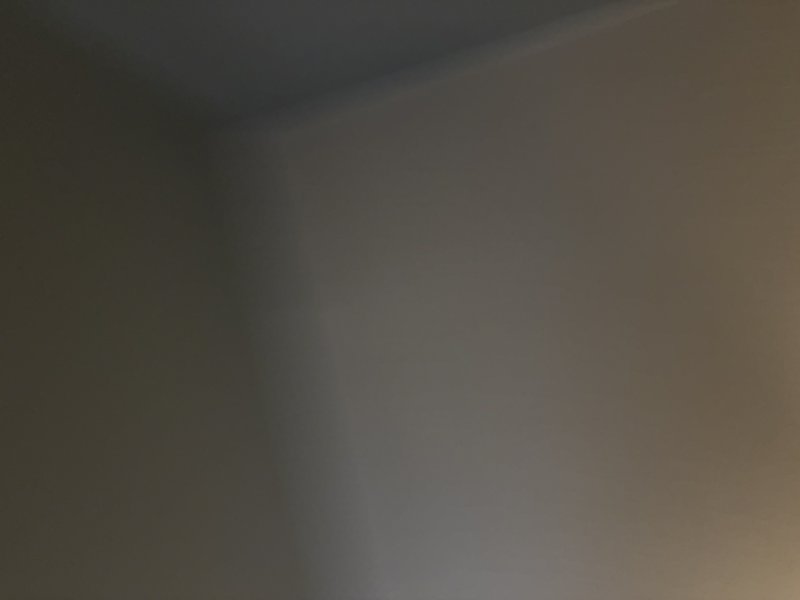 Blurry interior corner with neutral beige-gray walls and soft lighting.