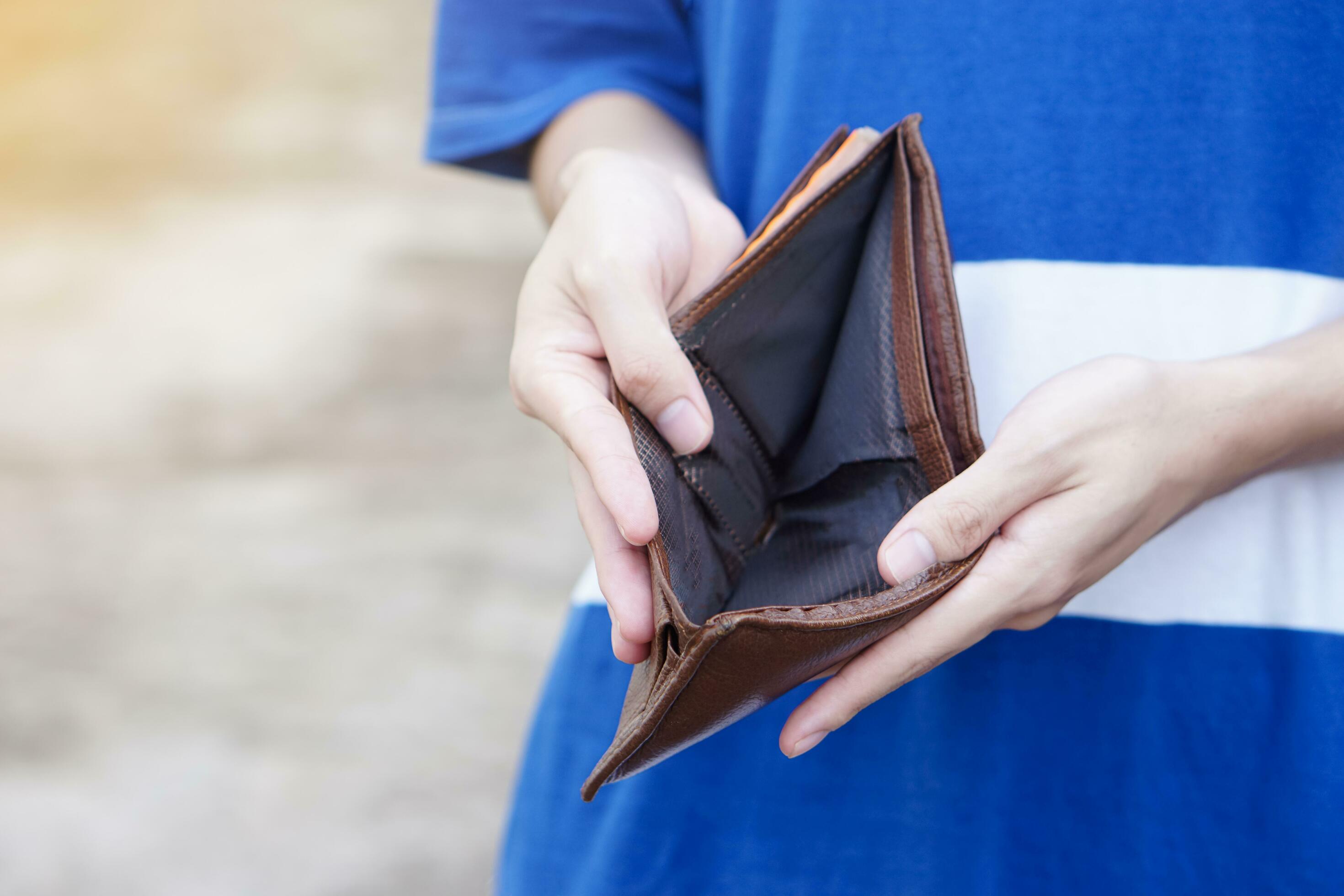 Close-up of a person in a blue shirt holding an open brown leather wallet.
