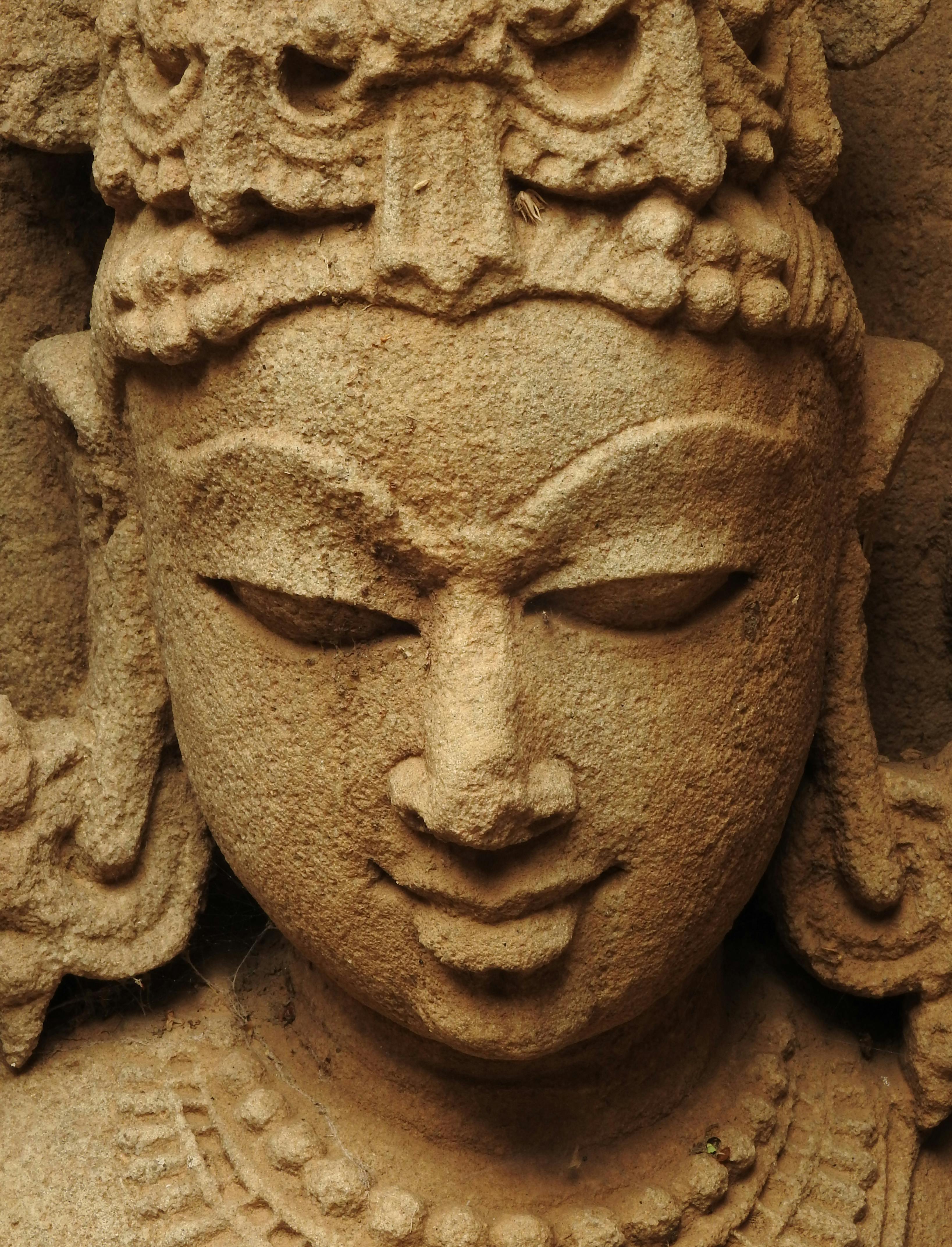Serene stone sculpture head with closed eyes and intricate headdress.
