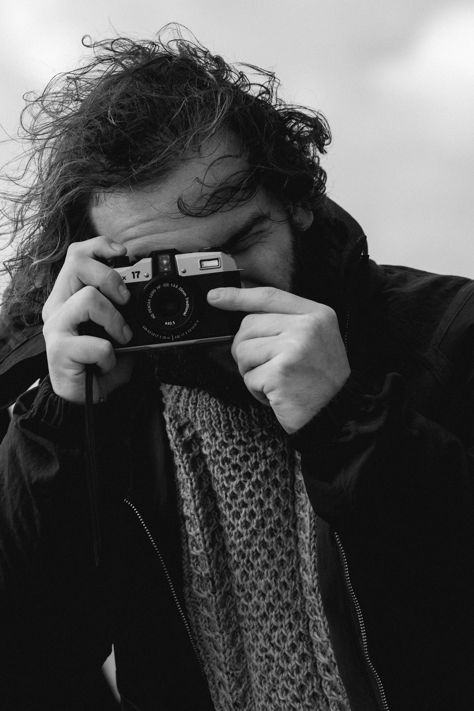 Man with a vintage camera up to eye in a moody black-and-white portrait.