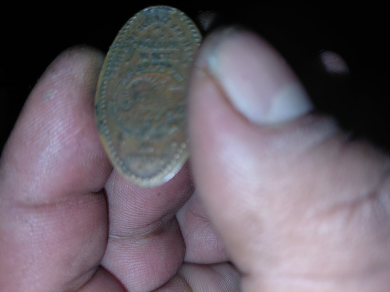 Close-up of a weathered coin held between fingers in low light