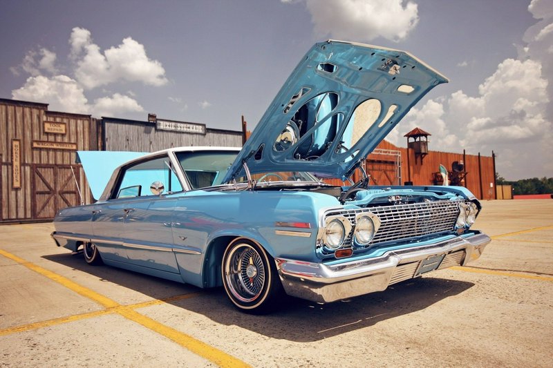 Shiny light-blue vintage car with its hood open at an outdoor car show on a sunny day