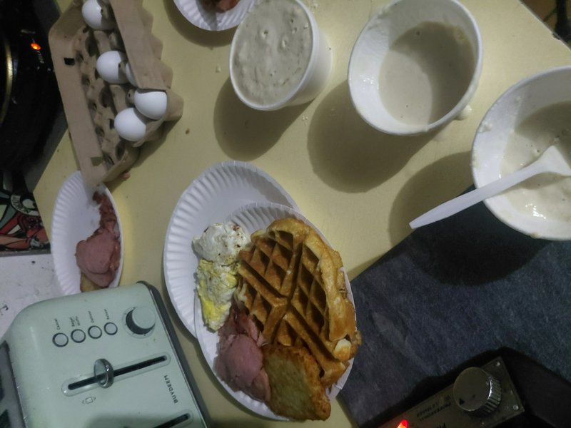 Plate with waffles, scrambled eggs, and meat slices on a kitchen counter with batter bowls and a ...