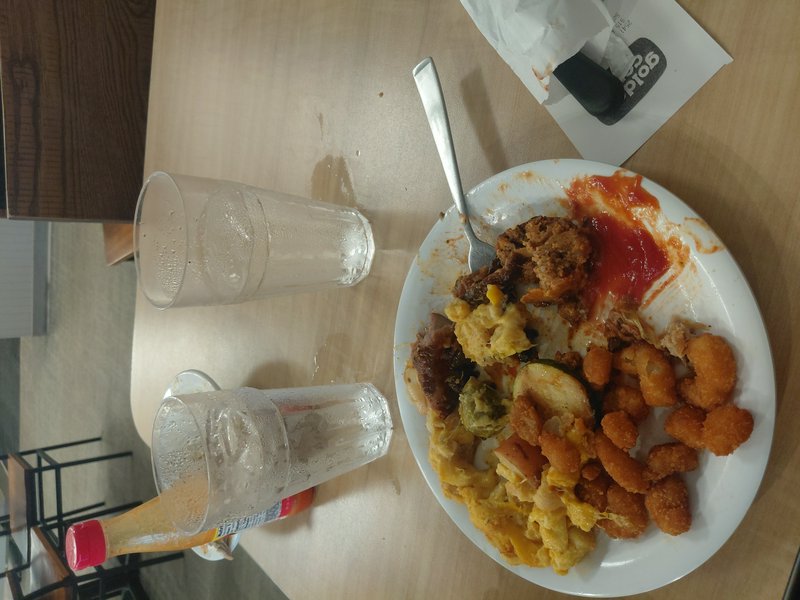 Partially eaten plate of casual American buffet food with two empty iced water glasses on a light...
