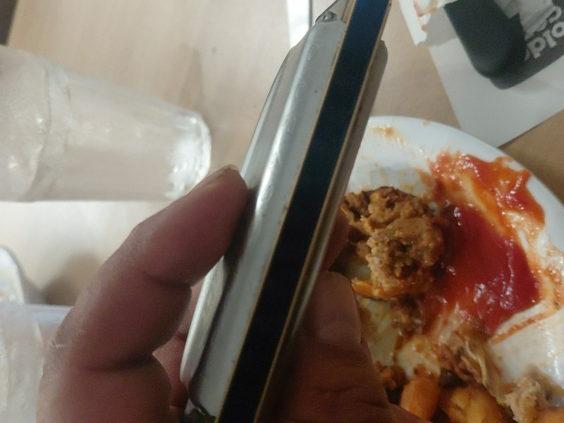 Hand holding a closed silver vintage flip phone above a plate of leftover fast food takeout and e...