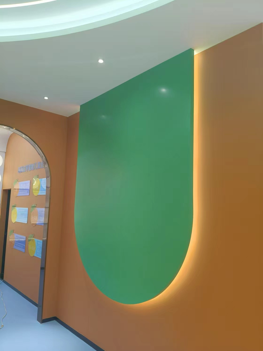Modern interior with a large green curved wall panel on an orange wall, edge-lit for a warm glow.