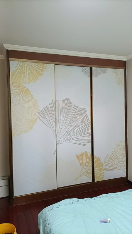 Sliding door wardrobe with white panels featuring gold and gray palm leaf patterns.