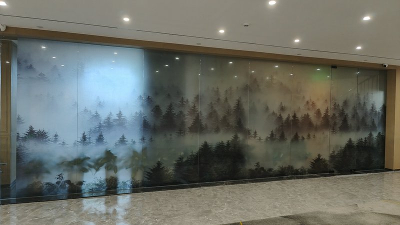 Glass wall mural of misty forest silhouettes across panels in an indoor lobby.