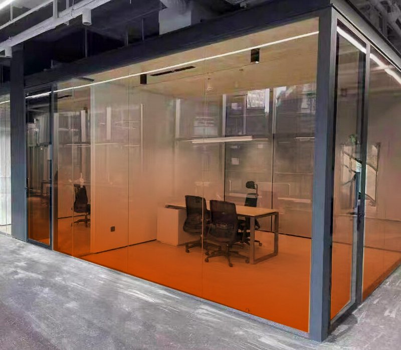 Glass-walled office pod with orange-tinted floor and modern desk chairs