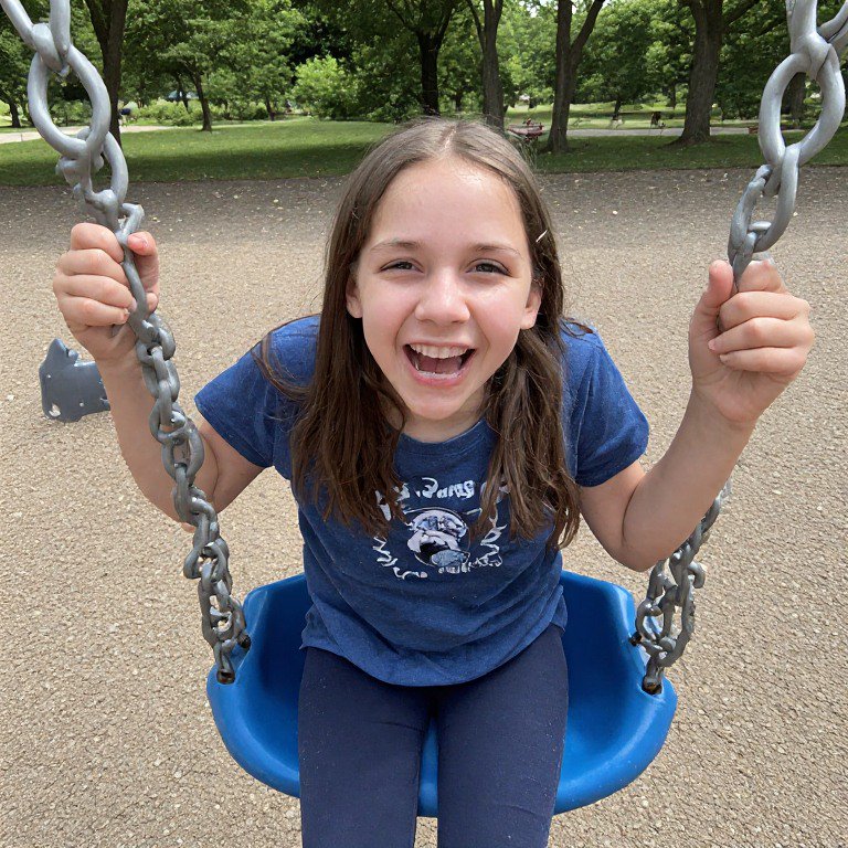 Smiling young girl on a blue swing at a park.