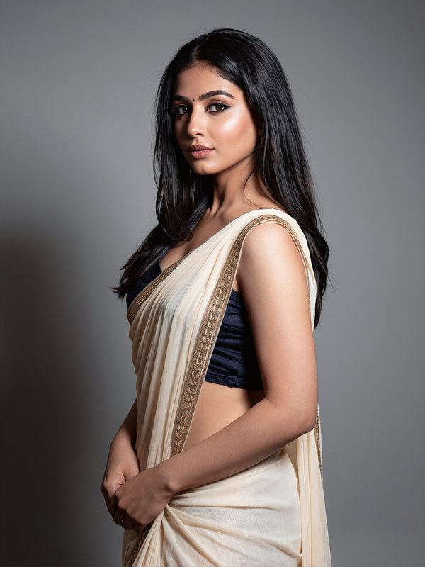 Studio portrait of a woman in a cream saree with a black blouse, posing gracefully.