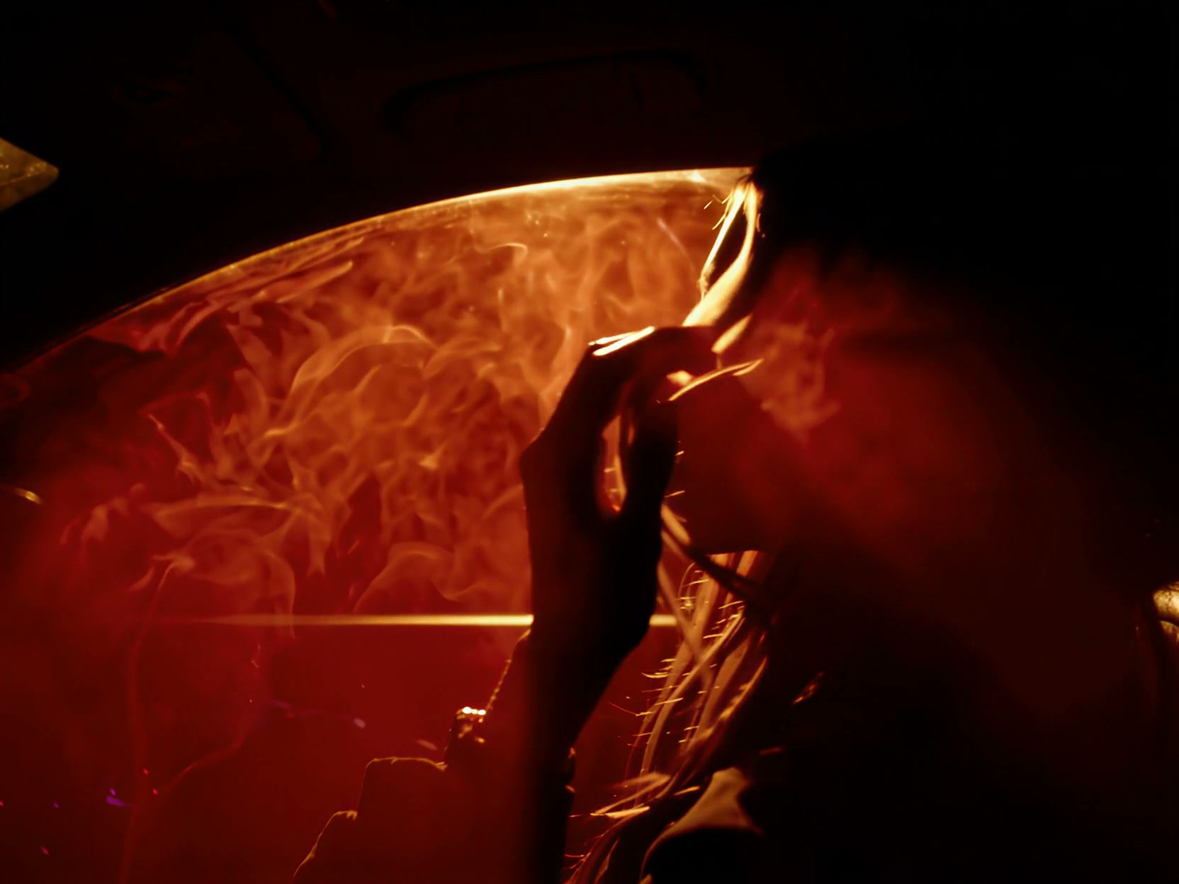 Silhouetted woman holding a cigarette inside a car, backlit by swirling warm orange-red smoke