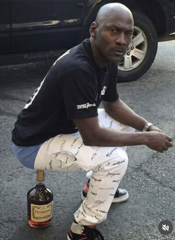 Man squatting on a street beside a bottle of Hennessy Cognac.